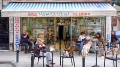 people sitting at tables in front of a store with dogs on leashes and one dog standing up