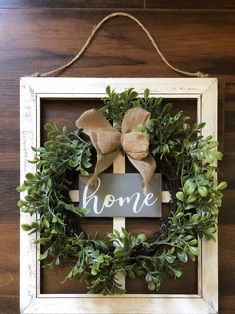 a wooden frame with a wreath and bow hanging on the wall above it that says home