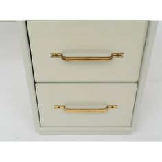 a white and gold file cabinet with two drawers on each side, one drawer has brass handles