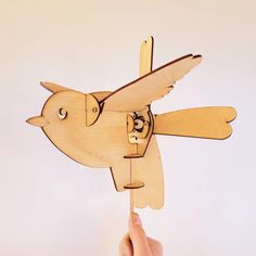 a hand holding a wooden toy with a bird on it's body and wings