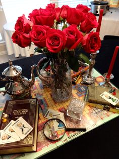 a table topped with lots of red roses next to a tea pot filled with books