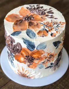 a white cake with orange and blue flowers on it sitting on a wooden table top