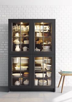 a black cabinet with glass doors filled with dishes and bowls on it next to a brick wall