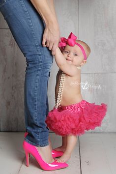 a woman holding the hand of a baby girl wearing pink shoes and a headband