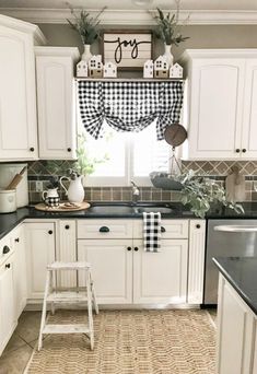 a kitchen with white cabinets and black counter tops is decorated with greenery on the window sill