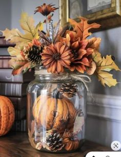 a glass jar filled with fake flowers and pine cones on top of a wooden table