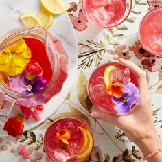 two people holding glasses filled with pink lemonade and flowered drinks on a table