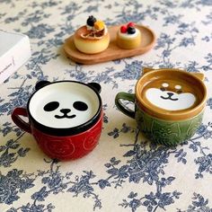 two small panda mugs sitting on top of a table next to plates with pastries