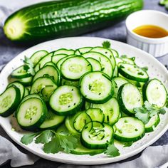 sliced cucumbers are arranged on a white plate next to dipping sauces and a green leafy garnish