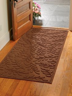 a door mat on the floor in front of an open wooden door with pink flowers