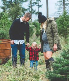 a man and woman holding hands while walking with a small child in a field full of trees