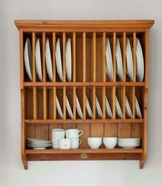 a wooden shelf filled with white dishes and cups on top of each other, next to a wall mounted dish rack