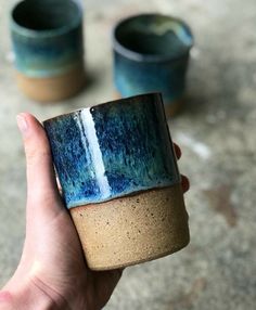 a hand holding a blue and brown coffee cup in front of two other mugs