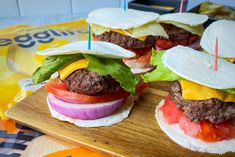 three hamburgers with lettuce, tomato and cheese on them sitting on a cutting board