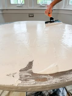 a person using a paint brush on a white round table in front of a window