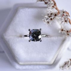 an engagement ring with a blue diamond sits on top of a white box next to some flowers