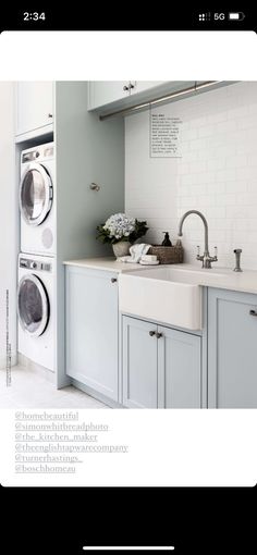 a white kitchen with grey cabinets and washer and dryer in front of the sink