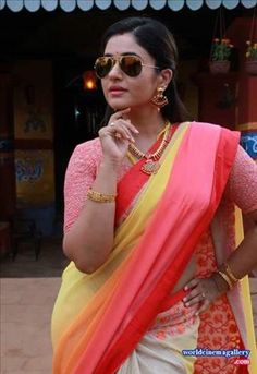 a woman wearing sunglasses and a sari standing in front of a building with her hand on her chin