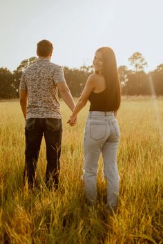 a man and woman holding hands while standing in the middle of a field with tall grass