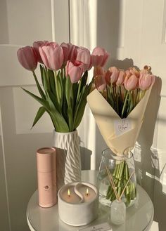 pink tulips are in vases and candles on a small table with a note