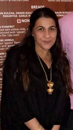 a woman standing in front of a sign wearing a necklace and black dress with gold accents