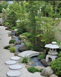 a garden with rocks and plants in it, along with a stone path that leads to a bridge