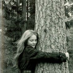 a woman leaning against a tree in the woods