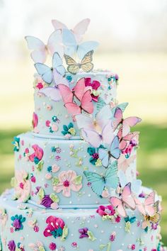 there is a blue cake with butterflies on it and pink flowers on the top tier