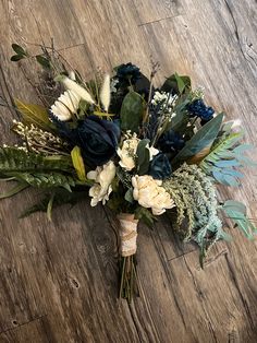 a bridal bouquet on the floor with blue and white flowers, greenery and feathers