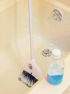 a white toilet brush sitting on top of a bath tub next to a blue liquid