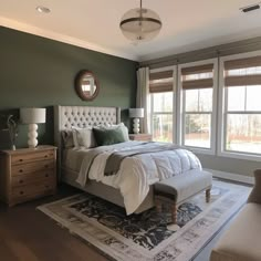 a bedroom with green walls and white bedding in the center, along with two windows