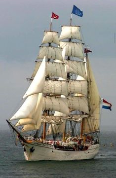 a large white sail boat sailing in the ocean with flags on it's mast