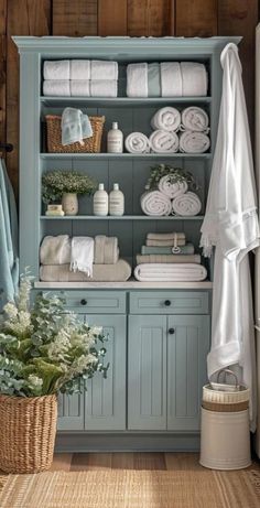 a bathroom with blue cabinets and white towels on it's shelves, next to a wicker basket filled with flowers