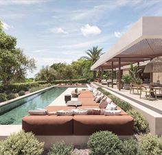 an outdoor living area with couches and tables next to a pool surrounded by greenery