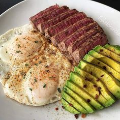 an egg, steak and avocado on a white plate with seasoning next to it