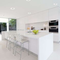 a white kitchen with lots of counter space and chairs around the island in front of it