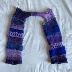 a purple and blue knitted scarf laying on top of a white bed coverlet