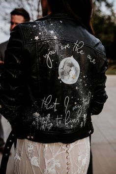 a woman wearing a black leather jacket with writing on it and a white lace skirt