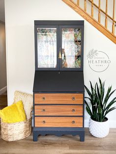 a wooden dresser sitting next to a plant in a living room under a stair case