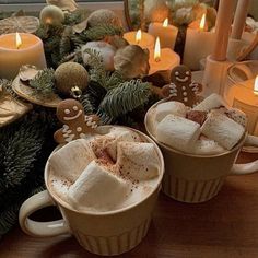 two cups filled with hot chocolate and marshmallows on a table next to candles