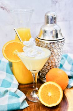 an orange drink with whipped cream and garnish in a glass next to two oranges