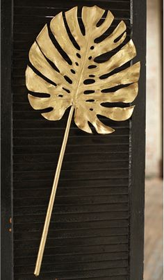 a gold leaf on top of a black shutter with a wooden stick sticking out of it