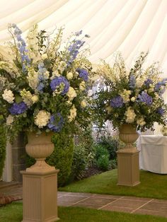 two large vases with flowers in them sitting on the grass near a table cloth