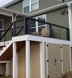 a house with a deck and stairs leading up to the second floor, next to a garage