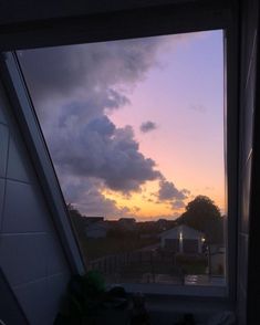 the sun is setting behind some clouds in the sky over a house and yard, as seen through a window