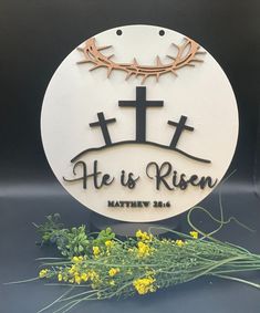 a white plaque with the words he is risen and a crown of crosses on it