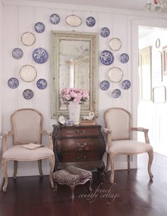 two chairs and a table in front of a mirror with plates on the wall behind it