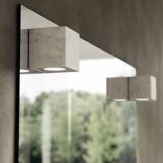 three square lights hanging from the side of a wall next to a window with trees in the background