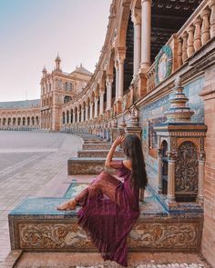 a woman sitting on a bench in front of a building and looking at the sky