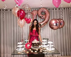 a woman standing in front of a table filled with cakes and cupcakes next to balloons